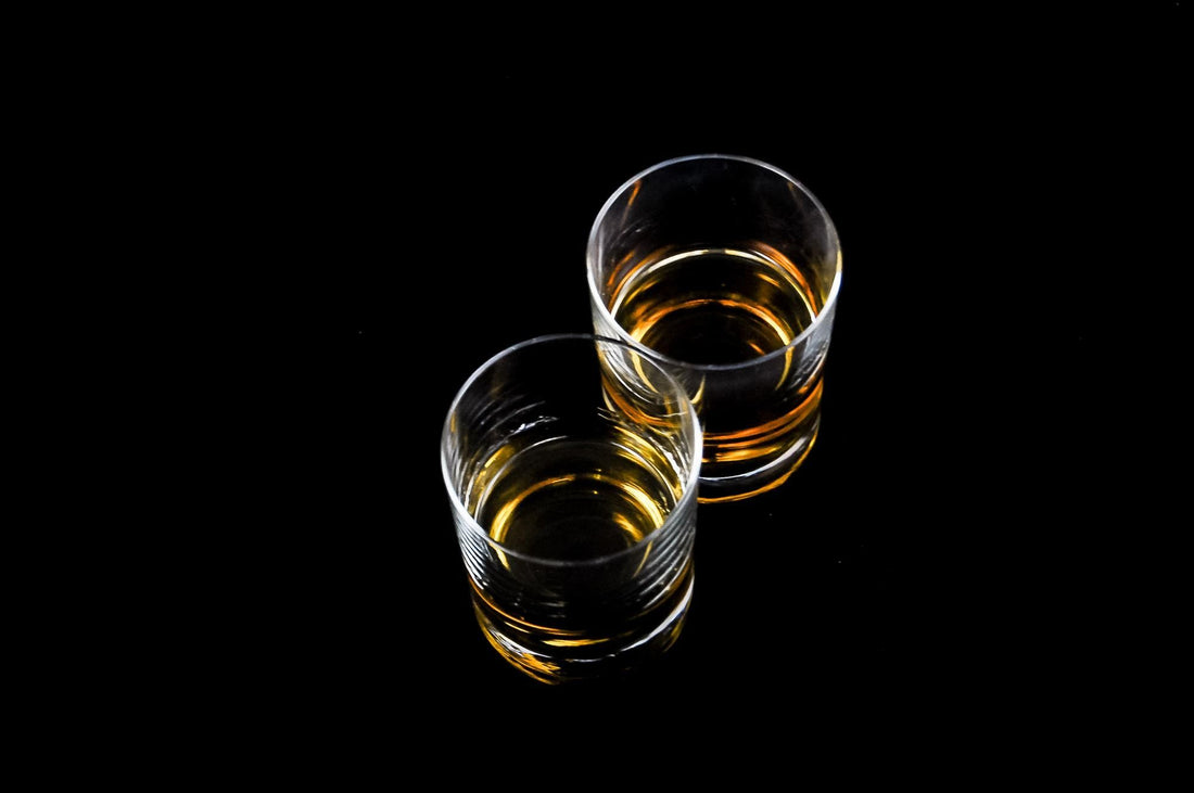 Glas met amberkleurige whiskycocktail op ijs in een tumbler, zoals een Godfather