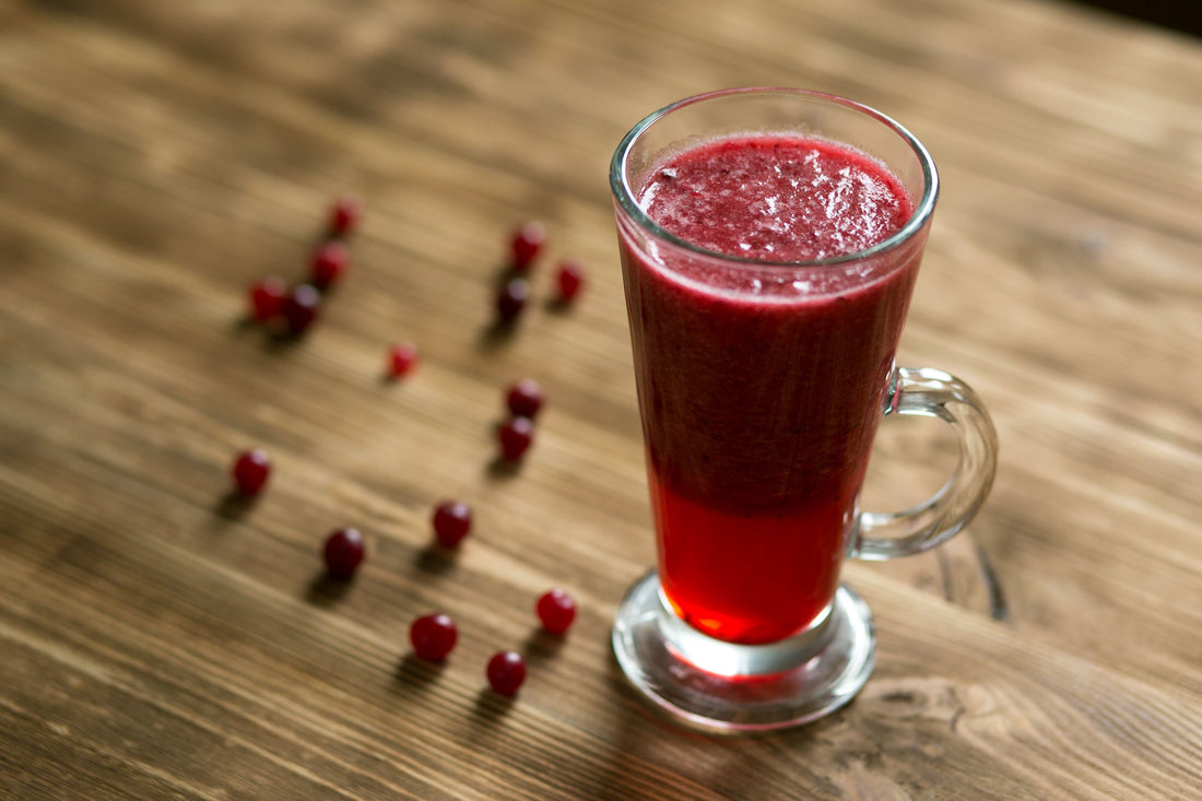 Hoog glas gevuld met dieprode cranberrydrank op een houten tafel, zoals bij een Sea Breeze cocktail