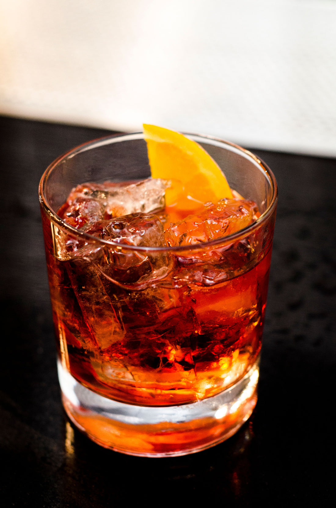 Negroni cocktail met ijs en een schijfje sinaasappel in een tumbler op een donkere ondergrond