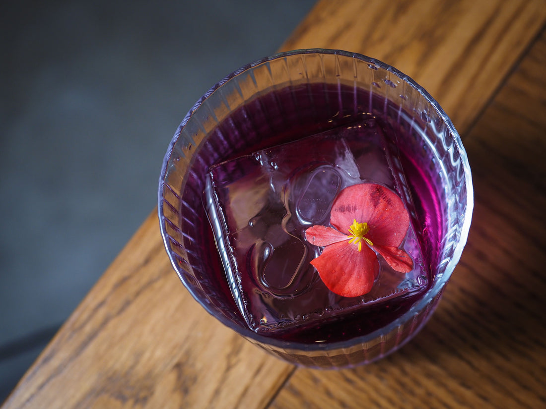 Violetkleurige cocktail in een elegant glas met bloemgarnering, in de stijl van een klassieke Aviation