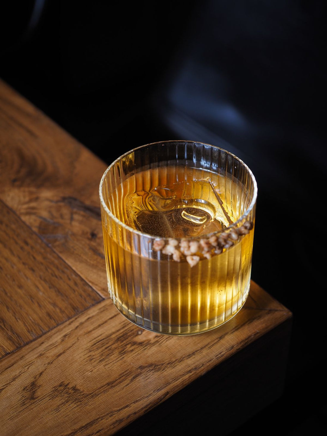 Glas met amberkleurige Dark 'n Stormy cocktail met ijsblokjes op een houten tafel