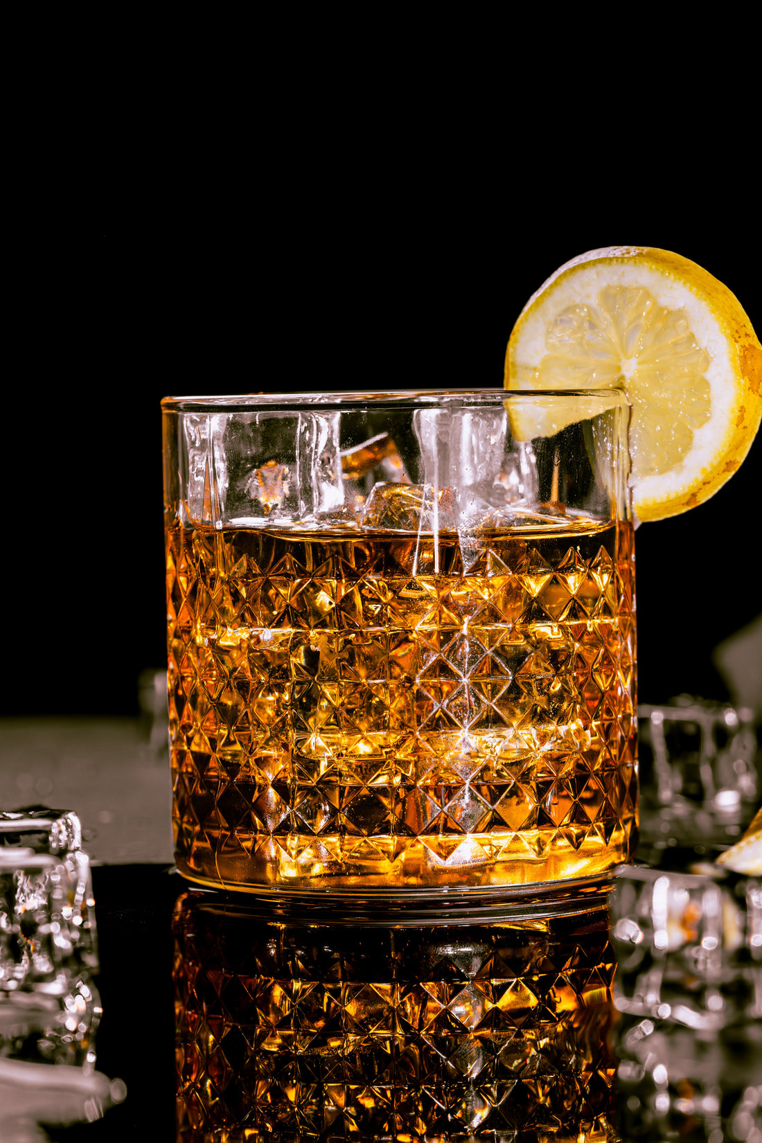Whiskycocktail met ijs en een schijfje citroen in een kristallen glas tegen een donkere achtergrond