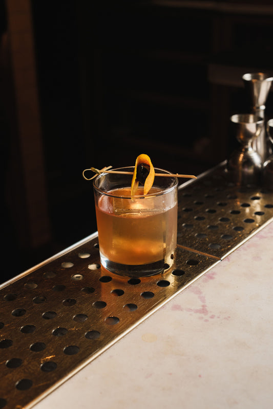 Klassieke Old Fashioned cocktail met sinaasappelzest en ijs in een tumbler op een sfeervol verlichte bar