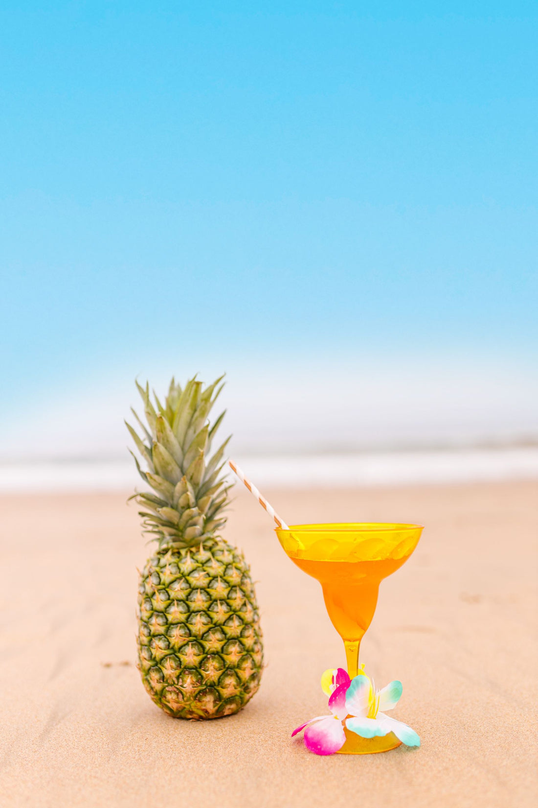 Tropische cocktail in een glas naast een verse ananas op het strand onder een blauwe lucht