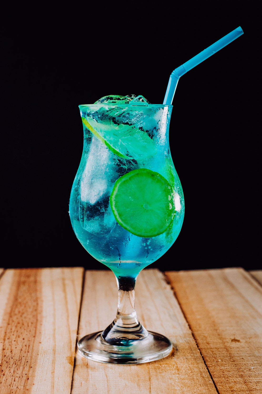 Knalblauwe Blue Lagoon cocktail in een longdrinkglas met ijsblokjes en een schijfje citrus als garnering