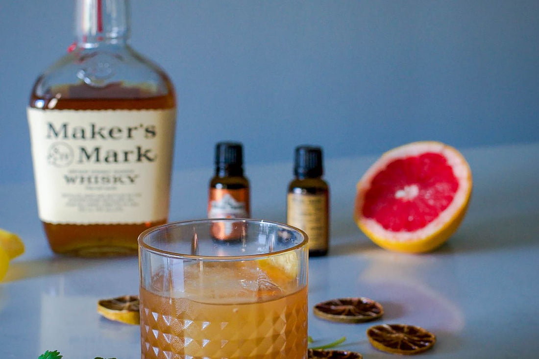Whiskycocktail in een tumbler met groot ijsblok en sinaasappelschil op een donkere houten bar